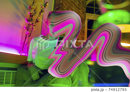 Cinematic portrait of stylish woman in neon lighted interior using a smartphone. The face is smeared, sucked into the phone. The concept of social network dependency Cinematic portrait of stylish woman in neon lighted interior using a smartphone. The face is smeared, sucked into the phone. The concept of social network dependency 74912793