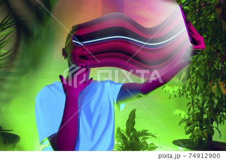 Cinematic portrait of stylish woman in neon lighted interior using a smartphone. The face is smeared, sucked into the screen. The concept of social network dependency 74912900