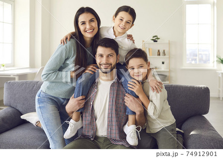 Portrait of happy mother, father and little children sitting on couch and smiling at camera 74912901