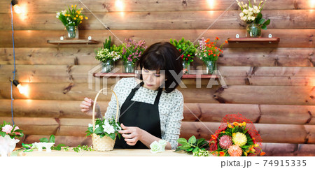 A worker in a black apron makes a beautiful bouquet of flowers and soap in a basket A worker in a black apron makes a beautiful bouquet of flowers and soap in a basket 74915335