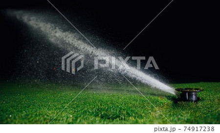 automatic lawn sprinkler spraying water over golf course green grass at night 74917238