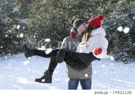 Loving couple in winter forest. Guy is holding his girlfriend in his arms and kiss. 74921126
