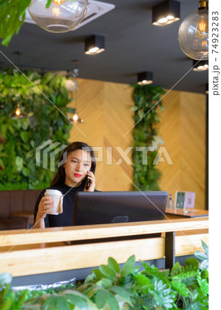 Young beautiful Asian businesswoman holding coffee while talking on the phone at the coffee shop Young beautiful Asian businesswoman holding coffee while talking on the phone at the coffee shop 74923283