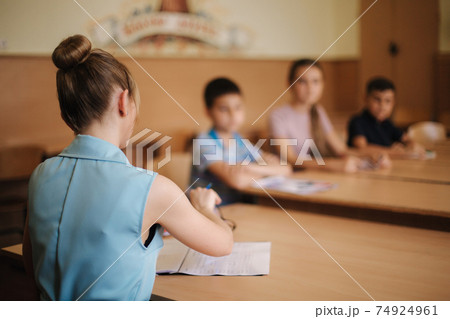 Education, elementary school. Learning and people concept - group of school kids with pens and notebooks writing test in classroom Education, elementary school. Learning and people concept - group of school kids with pens and notebooks writing test in classroom 74924961