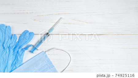 syringe for injections, nitrile gloves and a medical mask on light wooden table 74925116