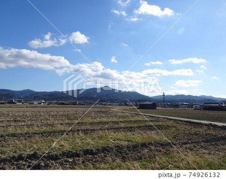 冬の田んぼと曲がりくねった農道と向こうに見える民家と山のある景色 冬の田んぼと曲がりくねった農道と向こうに見える民家と山のある景色 74926132