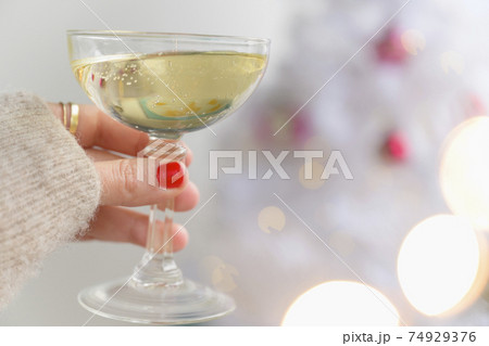 Hand holding champagne glass next to Christmas tree Hand holding champagne glass next to Christmas tree 74929376