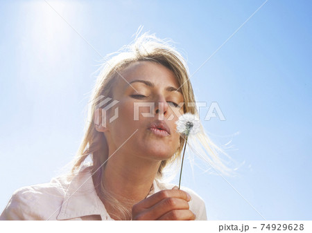 Blond woman blowing dandelion 74929628