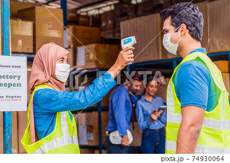 Muslim woman worker wearing surgical mask and Hijab uses Medical Digital Infrared Thermometer measure temperature to Indian man worker with safety clothes before start to work after warehouse reopen Muslim woman worker wearing surgical mask and Hijab uses Medical Digital Infrared Thermometer measure temperature to Indian man worker with safety clothes before start to work after warehouse reopen 74930064