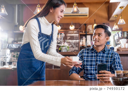 Asian Barista of Small business owner serving a cup of coffee to young customer at the table in coffee shop, Small business owner and startup in coffee shop and restaurant concept 74930172