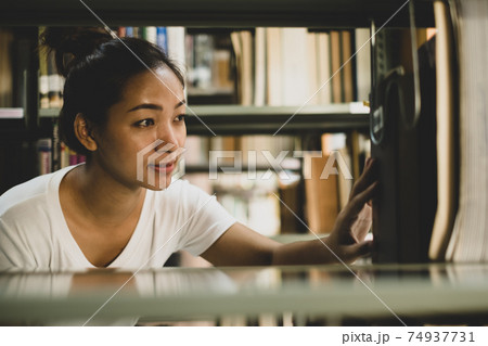 Young Asian women are searching for books and reading from the bookshelves in the college library to research and develop themselves in education Young Asian women are searching for books and reading from the bookshelves in the college library to research and develop themselves in education 74937731