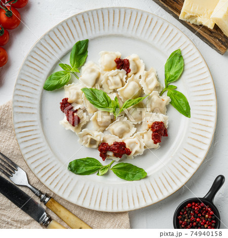 Ravioli pasta with mushroom cream sauce and cheese - Italian food style with basil parmesan and tomatoe on white plate, on white background , top view flat lay Ravioli pasta with mushroom cream sauce and cheese - Italian food style with basil parmesan and tomatoe on white plate, on white background , top view flat lay 74940158