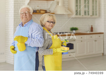 Ederly couple holding cleaning detergents and standing with their backs to each other in the kitchen Ederly couple holding cleaning detergents and standing with their backs to each other in the kitchen 74940399