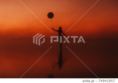 surreal silhouette of a girl with a balloon in her hand on the water 74941957