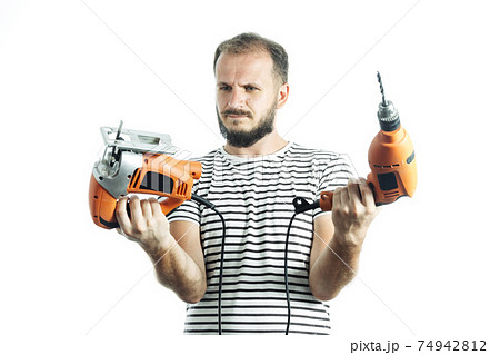 How to choose a power tool. Portrait of bearded handyman holding orange drill and electric jigsaw isolated on white 74942812