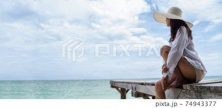 Happy Asian woman with straw hat relaxing and sitting on wooden terrace at a tropical beach. Summer Beach Vacation Concept. Happy Asian woman with straw hat relaxing and sitting on wooden terrace at a tropical beach. Summer Beach Vacation Concept. 74943377