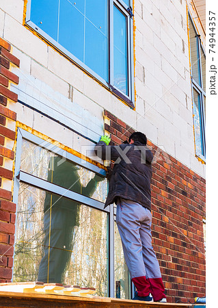 A man works with a drill, attaches thermal panels made of clinker A man works with a drill, attaches thermal panels made of clinker 74944357