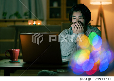 深夜リビングでホラー映画を見て怖がる若い女性 74944741