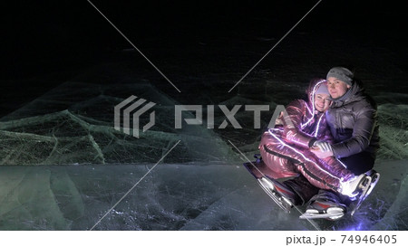 Young loving couple skating at ice rink at night. Man and woman kiss hug have fun learn to skate. Making love on ice. Ice illuminated backlit below. Young loving couple skating at ice rink at night. Man and woman kiss hug have fun learn to skate. Making love on ice. Ice illuminated backlit below. 74946405