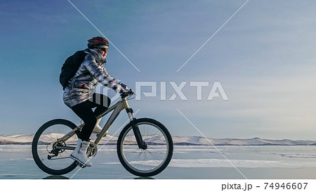 Woman is riding bicycle on the ice. Tires on bike are covered wi Woman is riding bicycle on the ice. Tires on bike are covered wi 74946607