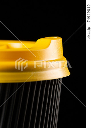 A fragment of a disposable corrugated cardboard cup with yellow lid on a black background. 74949019