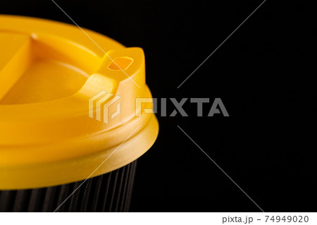 A fragment of a disposable corrugated cardboard cup with yellow lid on a black background. 74949020