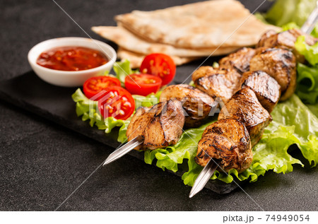 Two portions of shish kebab on a stone plate with salad. 74949054