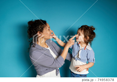 Smiling woman and her child touching each other's nose on blue background with copy space Smiling woman and her child touching each other's nose on blue background with copy space 74958378