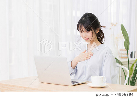 部屋でパソコンを使いながら胸に手を当てる若い女性 部屋でパソコンを使いながら胸に手を当てる若い女性 74966394