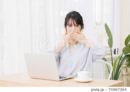 部屋でノートパソコンを使いながら口を隠す若い女性 部屋でノートパソコンを使いながら口を隠す若い女性 74967364