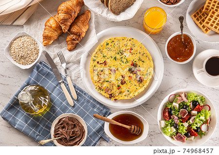 Broad assortment of food including omelette, croissants, salad, bread, oatmeal, jam, waffles, honey, choclate spread, coffee and orange juice served on a table 74968457