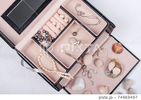 Sea jewelry collection in jewelry box on light marble background with seashells and pebbles. Pearl pendant necklace, pearl earrings and silver chains. Fashion flat lay, ocean summer jewelry 74969497