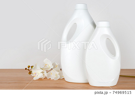 Bottles of detergent and fabric softener with white orchid flowers on wooden table. Containers of cleaning products. Liquid detergent and conditioner. Laundry day, cleaning concept. Bottles of detergent and fabric softener with white orchid flowers on wooden table. Containers of cleaning products. Liquid detergent and conditioner. Laundry day, cleaning concept. 74969515