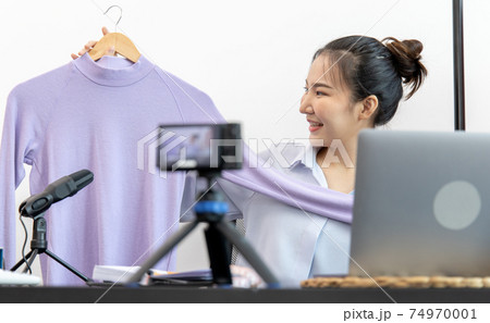 Young Asian women show off the clothes customers want to see through a live performance with a camera, Selling things through video recording or live shows via the Internet, Record live. Young Asian women show off the clothes customers want to see through a live performance with a camera, Selling things through video recording or live shows via the Internet, Record live. 74970001