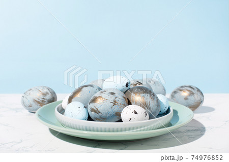 Easter blue golden eggs, quail eggs and plates on gray marble table. 74976852