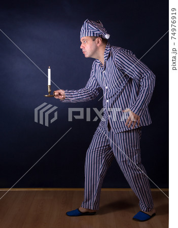 A frightened man with candle in pajamas 74976919