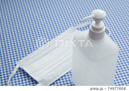 水色のギンガムチェックの布の上に置かれた手指消毒用アルコール液とマスク 水色のギンガムチェックの布の上に置かれた手指消毒用アルコール液とマスク 74977608