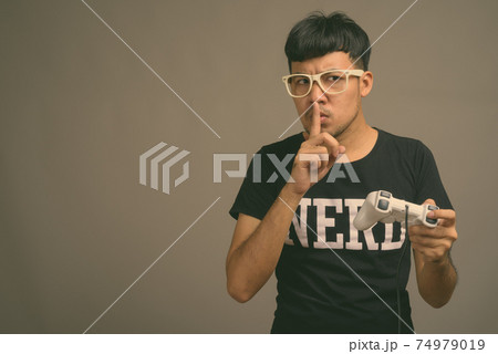 Young Asian nerd man wearing eyeglasses against gray background Young Asian nerd man wearing eyeglasses against gray background 74979019