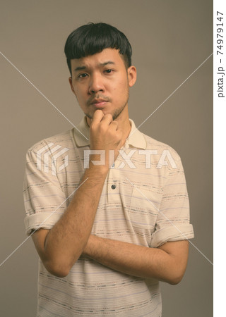 Portrait of young Asian man against gray background 74979147