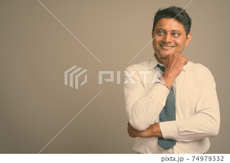 Portrait of young handsome Indian man against plain studio background 74979332