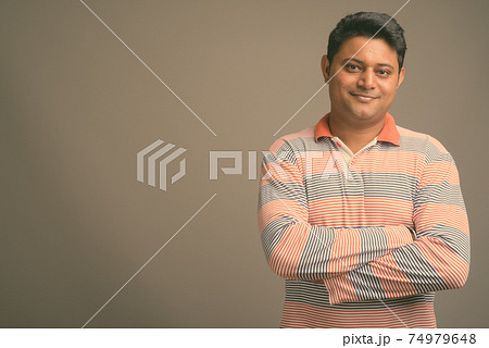 Portrait of young handsome Indian man against plain studio background 74979648