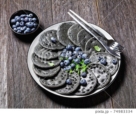 black sweet pancakes served with berries and mint 74983334