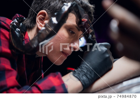 Tattoo artist with short hair a young girl with tattoos on her face and body and piercings works in a tattoo parlor Tattoo artist with short hair a young girl with tattoos on her face and body and piercings works in a tattoo parlor 74984870