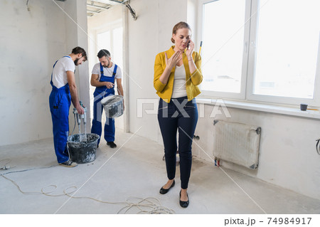 Woman uses phone in room with repairers 74984917