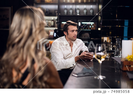 a man and a woman sitting at a table at the bar, the face of a man, the back of a blonde woman with long hair 74985058