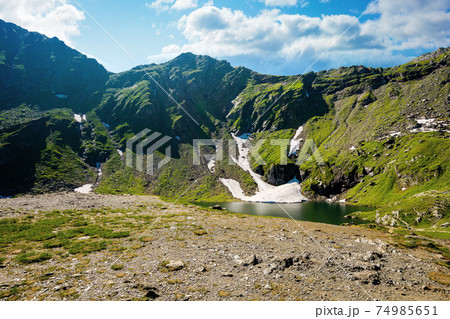 balea lake in fagaras mountain of romania. beautiful landscape in summertime. rocky slopes with grass in snow. sunny weather with fluffy clouds on the sky. popular travel destination 74985651