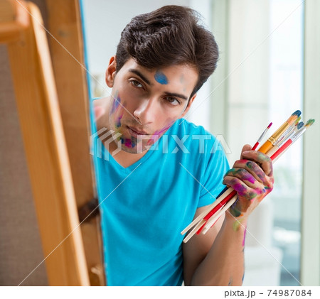 Young funny artist working on new painting in his studio Young funny artist working on new painting in his studio 74987084