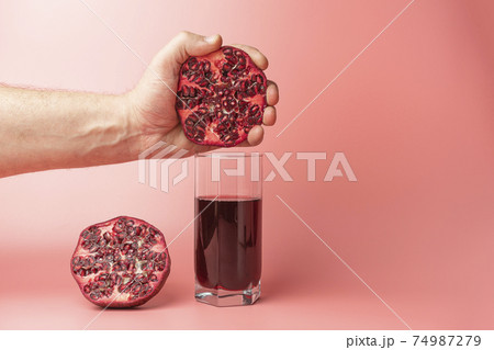 a hand squeezing juice from a pomegranate into a glass a hand squeezing juice from a pomegranate into a glass 74987279