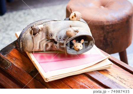 Close-up mice and brown shoes on wooden chest. Mouse sleeping in old torn brown shoe. Figurines in street market Close-up mice and brown shoes on wooden chest. Mouse sleeping in old torn brown shoe. Figurines in street market 74987435