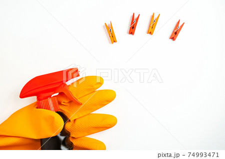 Black cleansing spray in hand in orange glove and multicolored clothespins on white background. Cleaning, cleanliness and household chemicals concept. Copy space Black cleansing spray in hand in orange glove and multicolored clothespins on white background. Cleaning, cleanliness and household chemicals concept. Copy space 74993471